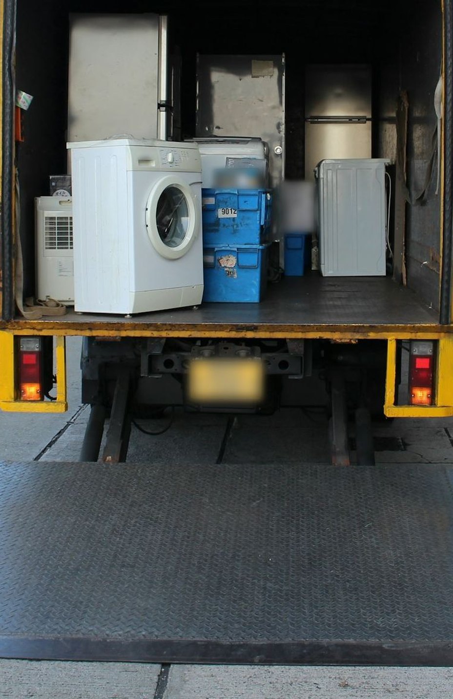 Een wasmachine en koelkasten in de laadruimte van een bakwagen met de laadklep neer