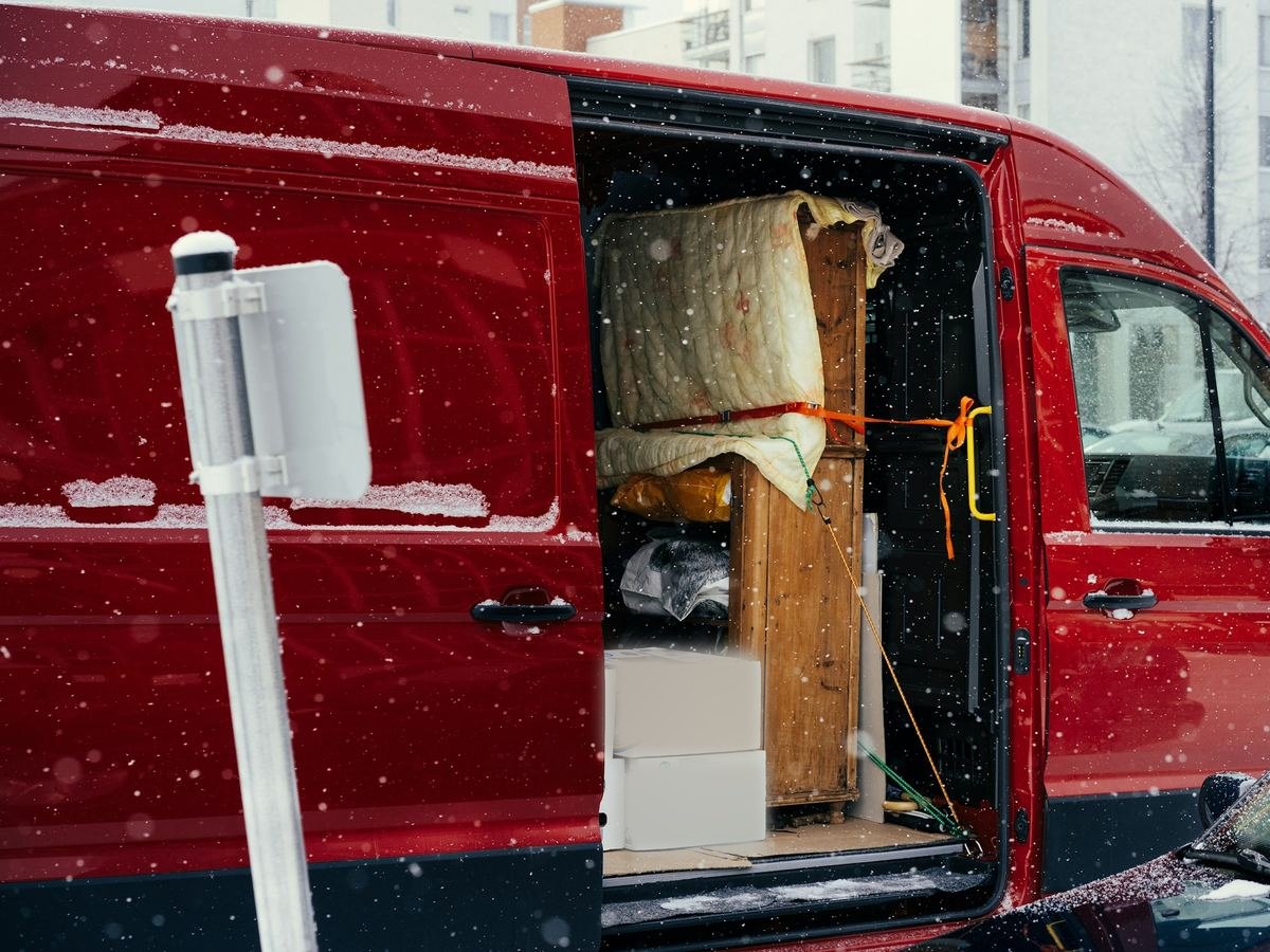 Een kast in een verhuisdeken, vastgesjord in een rode bestelwagen met de schuifdeur open